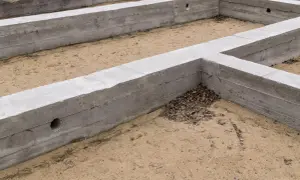 Fundamenty budynku w stanie zero, betonowe ściany fundamentowe tworzą zarys przyszłego domu na piaszczystym podłożu.