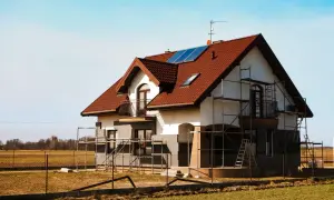Dom w budowie z rusztowaniami, panelami słonecznymi i anteną. Prąd docelowy na czas budowy zapewnia energię do prac.