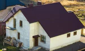 Nowy dom w zabudowie zagrodowej z ciemnobrązowym dachem, w trakcie budowy.