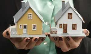 Dwie makiety domów w dłoniach. Jedna żółta, druga biała. Rozważasz budowę domu na działce z istniejącym domem?