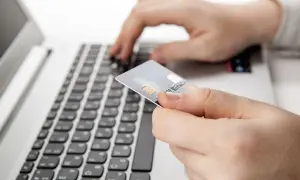 Dłoń trzyma kartę płatniczą nad klawiaturą laptopa. Czy nazwa odbiorcy w przelewie ma znaczenie?