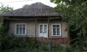 Stary dom z lat 80. z falistym dachem i zarośniętym ogrodem. Pozwolenie na użytkowanie domu z lat 80. jest widoczne na jego fasadzie.