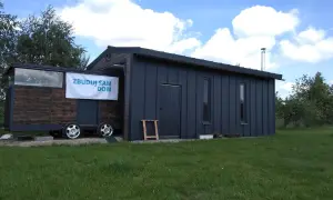Mobilny garaż bez pozwolenia 70m2, z drewnianą częścią na przyczepie i ciemnoszarą, nowoczesną bryłą.