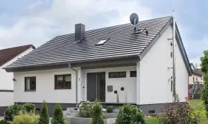 Nowoczesny dom z białymi ścianami i ciemnym dachem o kącie nachylenia dachu 35 stopni. Przed wejściem schody i zadbane rośliny.