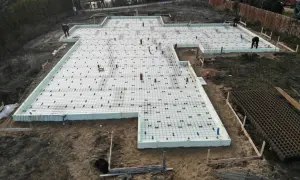 Prace na działce budowlanej: fundament z płytami izolacyjnymi i zbrojeniem, gotowy do zalania betonem. Glina wokół placu budowy.