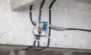 Widoczne przyłącze energetyczne od skrzynki sąsiada, z przewodami wchodzącymi do białej puszki instalacyjnej na betonowej belce.
