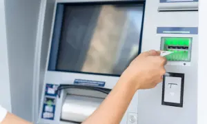Dłoń wsuwa kartę do bankomatu.