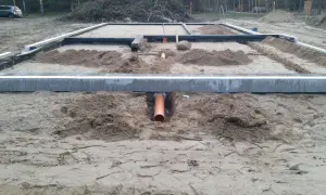 Pomarańczowa rura kanalizacyjna przechodzi przez wykop pod fundamentem, zapewniając przepust wody.