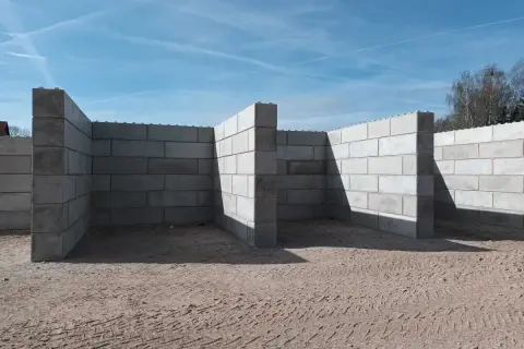 Betonowy murek oporowy w kształcie litery L, tworzący skarpy na placu budowy.