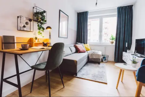 Przytulny salon z biurkiem, kanapą i roślinami. Idealne miejsce do pracy i relaksu, gdzie można też pomyśleć o podatku od wynajmu mieszkania.