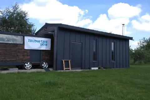 Mobilny garaż bez pozwolenia 70m2, z drewnianą częścią na przyczepie i ciemnoszarą, nowoczesną bryłą.