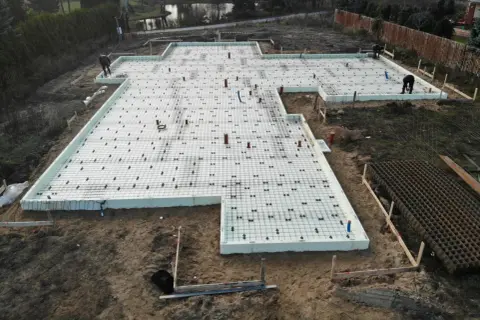 Prace na działce budowlanej: fundament z płytami izolacyjnymi i zbrojeniem, gotowy do zalania betonem. Glina wokół placu budowy.