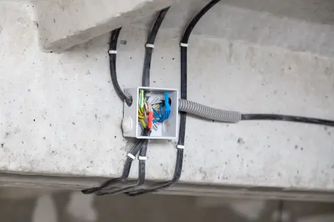 Widoczne przyłącze energetyczne od skrzynki sąsiada, z przewodami wchodzącymi do białej puszki instalacyjnej na betonowej belce.