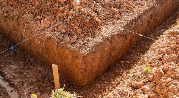 Wyznaczone wykopy pod fundamenty, z widocznymi nićmi wyznaczającymi linie i drewnianym palikiem.