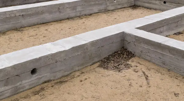 Fundamenty budynku w stanie zero, betonowe ściany fundamentowe tworzą zarys przyszłego domu na piaszczystym podłożu.