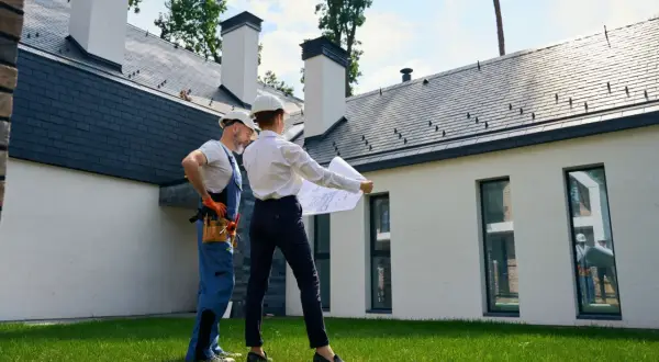 Architekt i budowlaniec omawiają plany przed nowoczesnym domem w budowie. Mieszkanie w domu bez odbioru to wyzwanie, ale i szansa na stworzenie wymarzonego wnętrza.