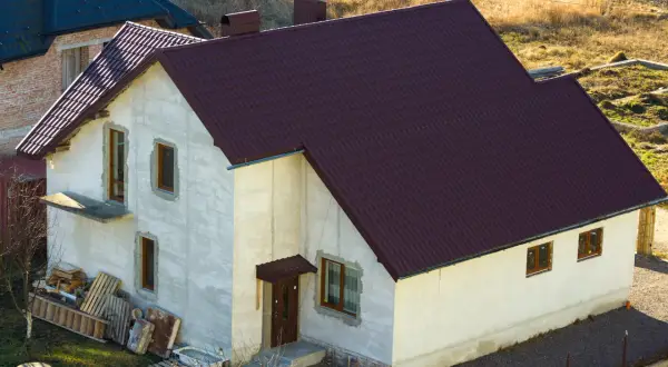Nowy dom w zabudowie zagrodowej z ciemnobrązowym dachem, w trakcie budowy.