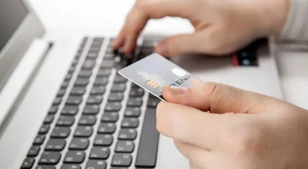 Dłoń trzyma kartę płatniczą nad klawiaturą laptopa. Czy nazwa odbiorcy w przelewie ma znaczenie?