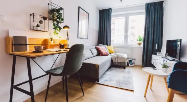 Przytulny salon z biurkiem, kanapą i roślinami. Idealne miejsce do pracy i relaksu, gdzie można też pomyśleć o podatku od wynajmu mieszkania.