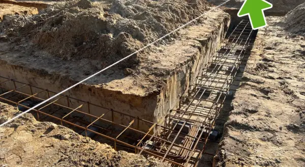 Wykonano wykopy pod fundamenty, w których widać zbrojenie. W tle plac budowy z hałdami ziemi i elementami konstrukcji. Widać ławy ciesielskie.