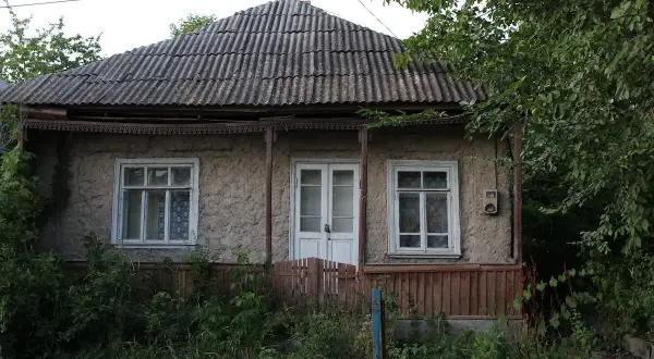 Stary dom z lat 80. z falistym dachem i zarośniętym ogrodem. Pozwolenie na użytkowanie domu z lat 80. jest widoczne na jego fasadzie.