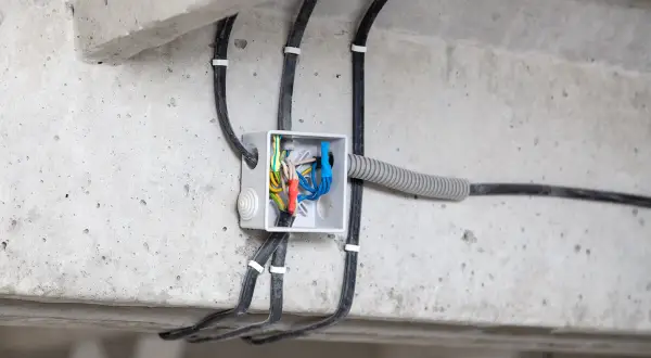 Widoczne przyłącze energetyczne od skrzynki sąsiada, z przewodami wchodzącymi do białej puszki instalacyjnej na betonowej belce.