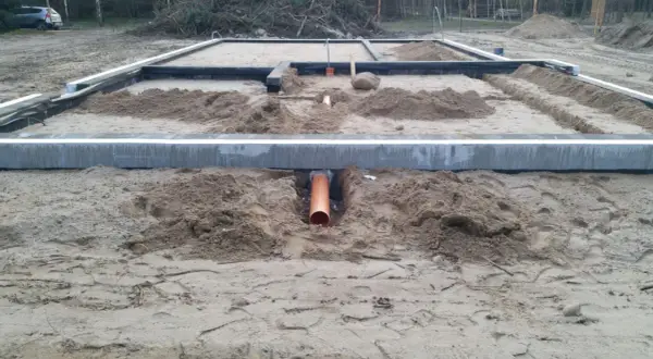 Pomarańczowa rura kanalizacyjna przechodzi przez wykop pod fundamentem, zapewniając przepust wody.