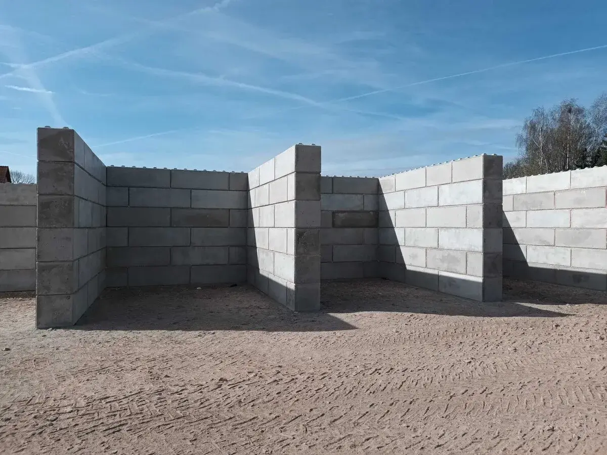 Betonowy murek oporowy w kształcie litery L, tworzący skarpy na placu budowy.