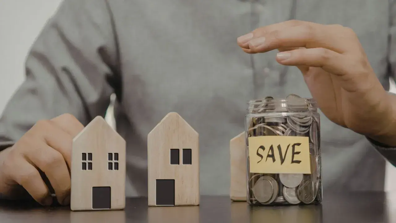 Dwa drewniane domki i słoik z monetami z napisem "SAVE". Czy mieszkanie może być wkładem własnym?