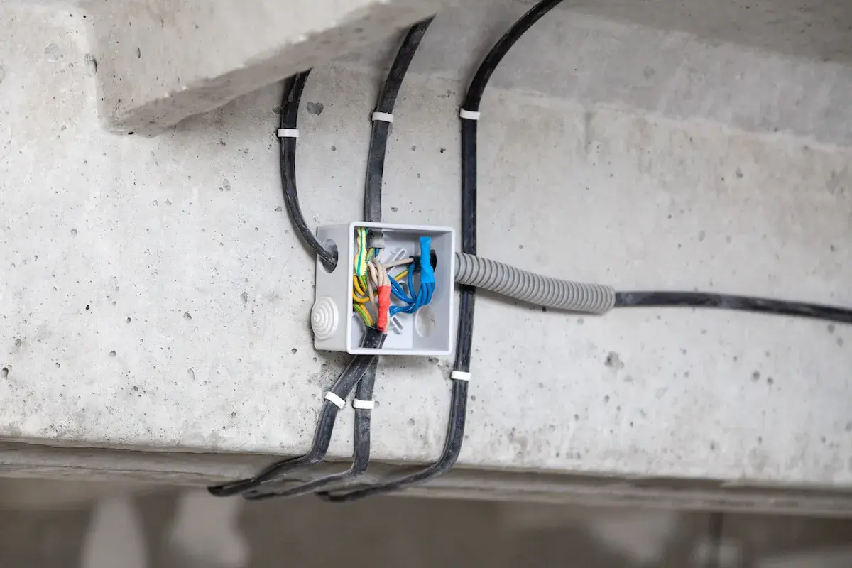 Widoczne przyłącze energetyczne od skrzynki sąsiada, z przewodami wchodzącymi do białej puszki instalacyjnej na betonowej belce.