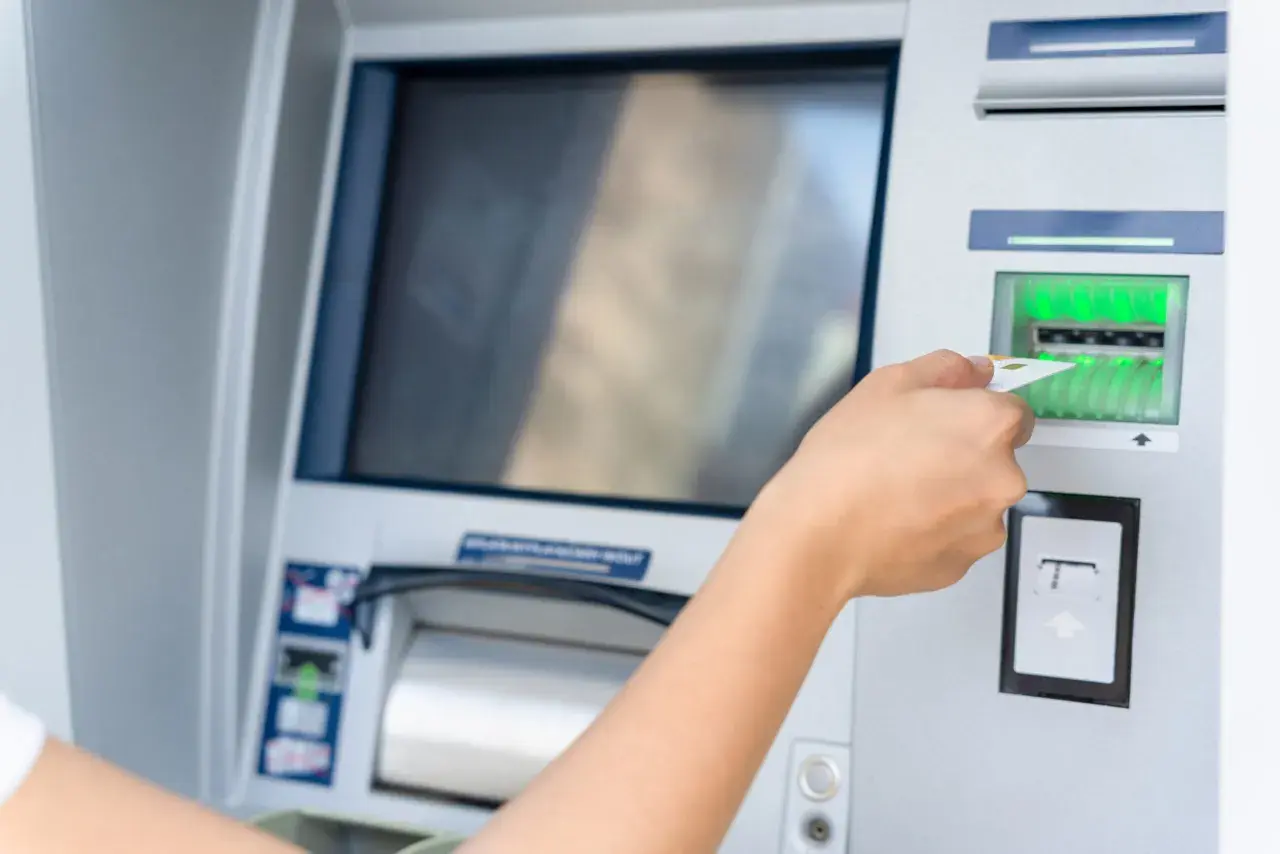 Dłoń wsuwa kartę do bankomatu.