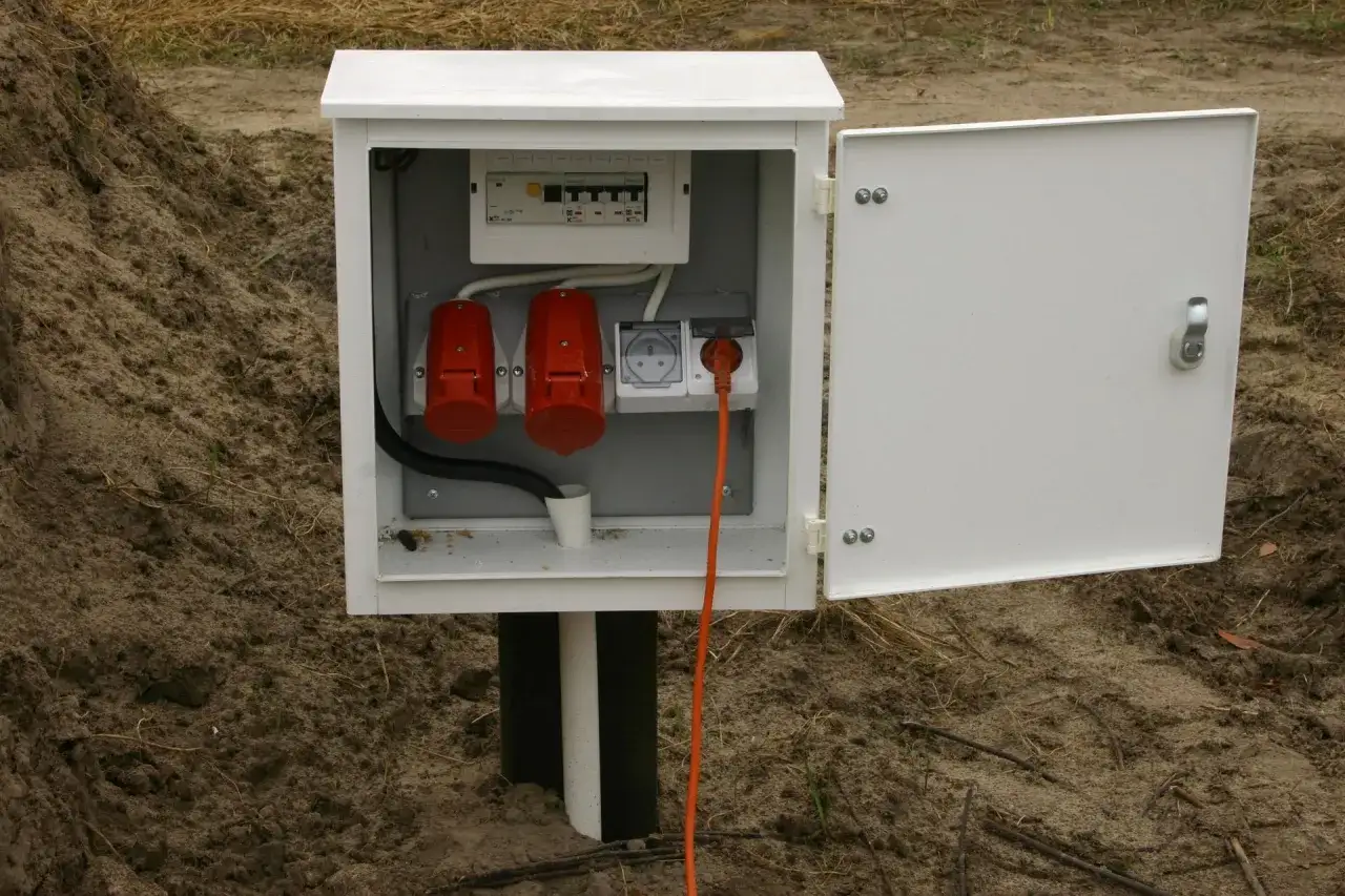Skrzynka elektryczna z zabezpieczeniami i gniazdami, zapewniająca prąd docelowy na czas budowy. Pomarańczowy kabel wychodzi z gniazda.