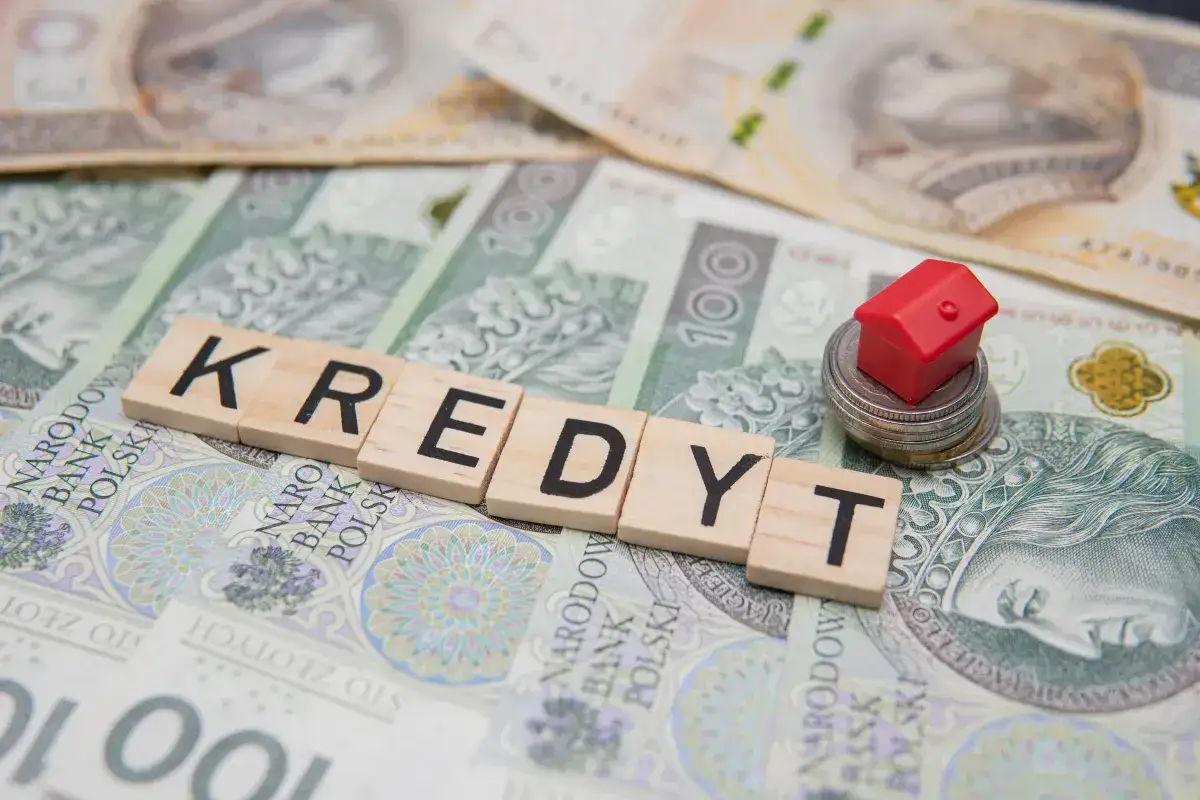 Kredyt na dom w czasie wojny? Na stosie monet i banknot&oacute;w 100 zł leży czerwony domek.