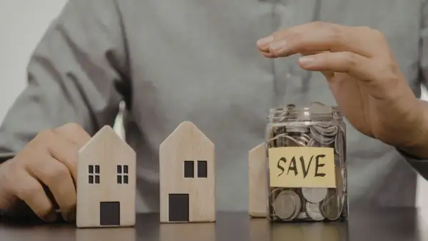Dwa drewniane domki i słoik z monetami z napisem "SAVE". Czy mieszkanie może być wkładem własnym?