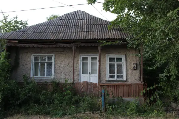 Stary dom z lat 80. z falistym dachem i zarośniętym ogrodem. Pozwolenie na użytkowanie domu z lat 80. jest widoczne na jego fasadzie.