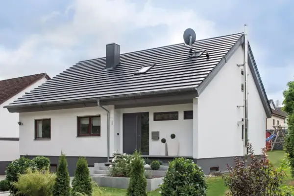 Nowoczesny dom z białymi ścianami i ciemnym dachem o kącie nachylenia dachu 35 stopni. Przed wejściem schody i zadbane rośliny.
