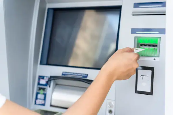 Dłoń wsuwa kartę do bankomatu.